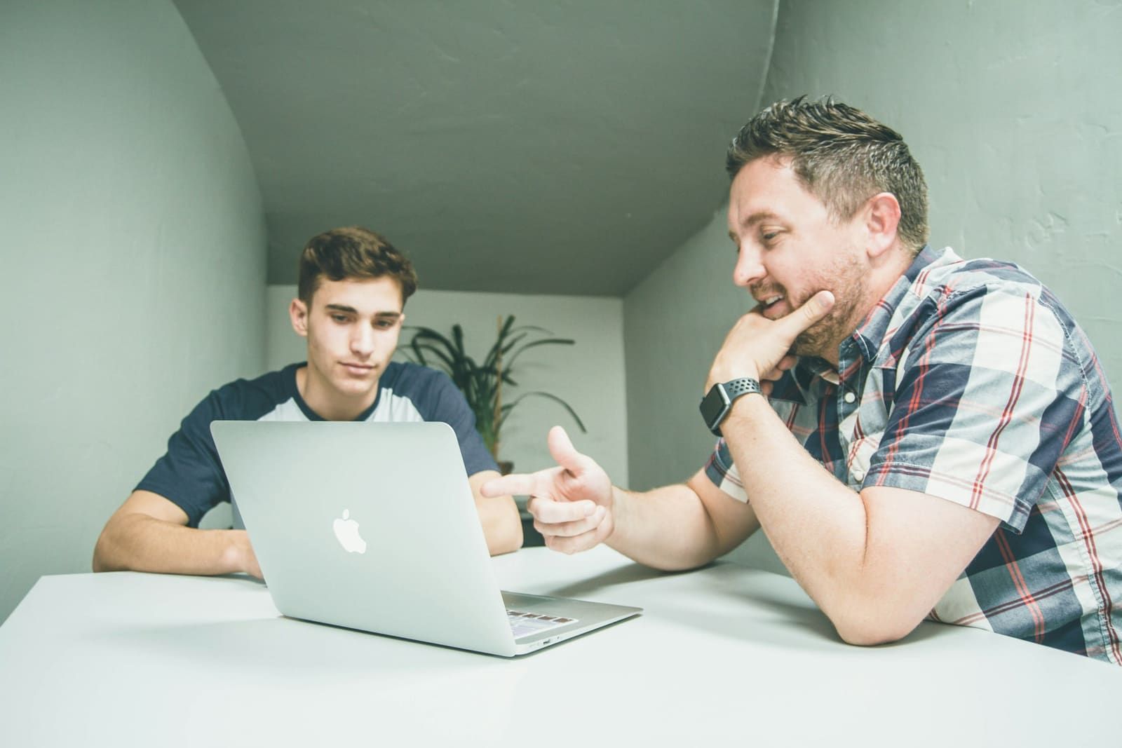 A mentor points at a laptop screen while a younger developer follows along.