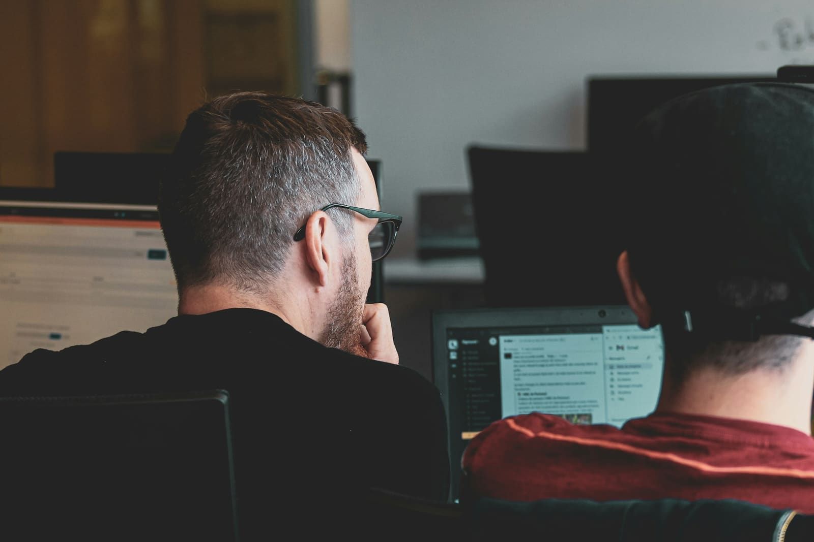 Two developers seen from behind while one talks the other through something on a laptop.