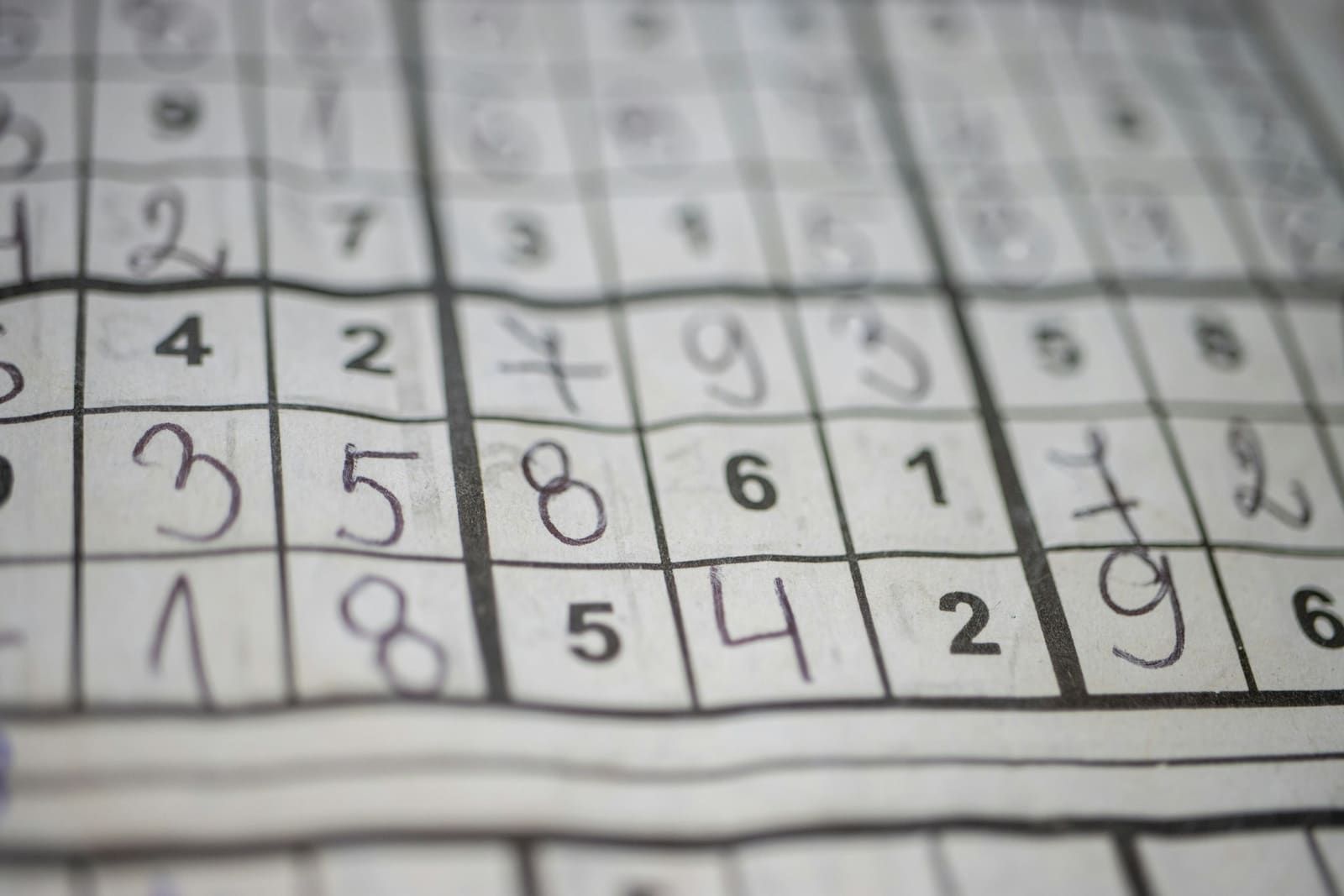 A close-up of a newspaper sudoku grid, partly filled in by hand.