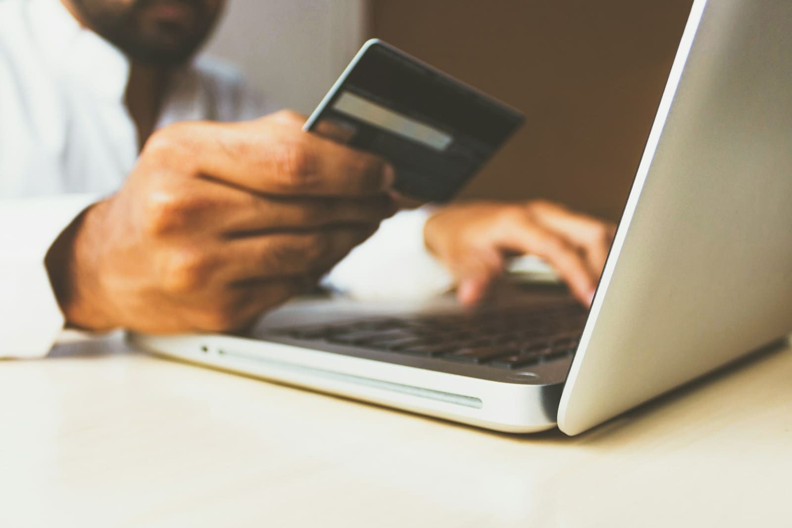 A man holds a payment card in one hand while typing on a laptop.